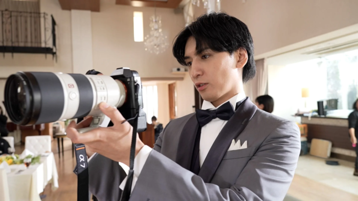 スーツと蝶ネクタイの男性がカメラを構える