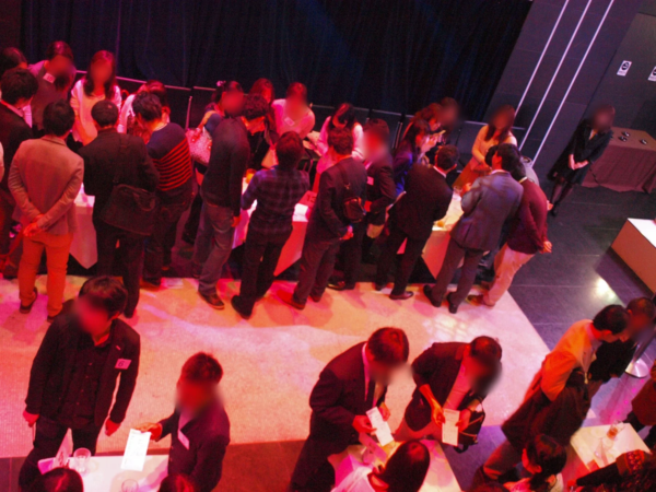 赤い照明が特徴的な屋内のイベント会場で、多くの人々が立ち話をしている様子