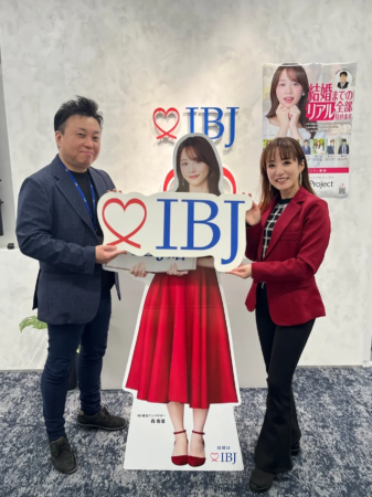 IBJのロゴがある場所で、男性と女性が「IBJ婚活アンバサダー森香澄」の等身大パネルを持って笑顔で写っている