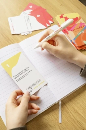 木製のテーブルで、一人の人物がノートにペンで書き込みをしています。