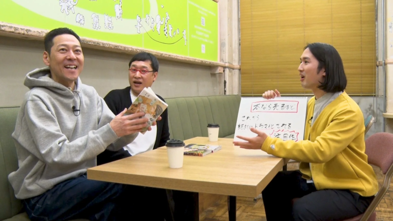 3人の男性がカフェのような空間で書籍やエンターテイメントについて活発に議論している様子