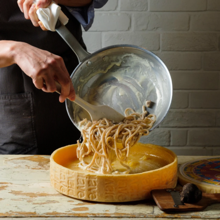 シェフがフライパンからクリームソースのスパゲッティを大きなチーズの塊の中へ移す様子