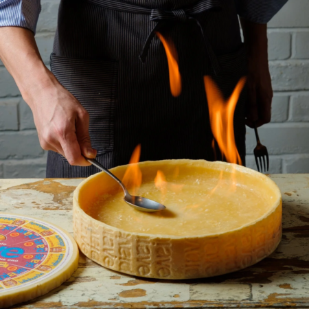 大きなチーズの塊の中で炎を使ってチーズを溶かす料理人