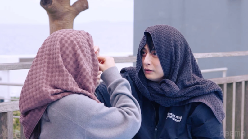 屋外で男女がタオルを頭に巻いて寄り添っている親密な雰囲気の様子です。