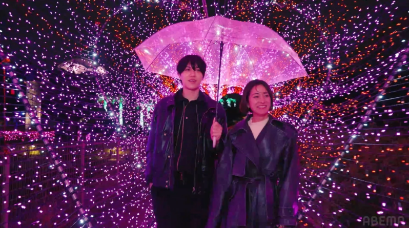 イルミネーションの光のトンネルを傘を差して歩くカップル