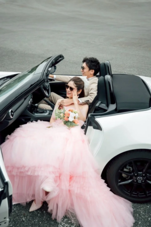 白いオープンカーに乗るウェディングカップル