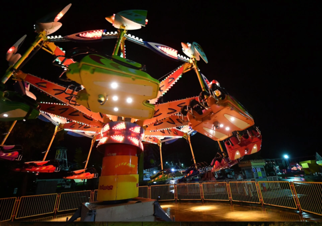 夜の遊園地の回転式アトラクションがライトアップされています