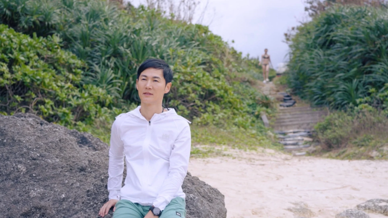 ビーチで岩に座る石丸伸二さん