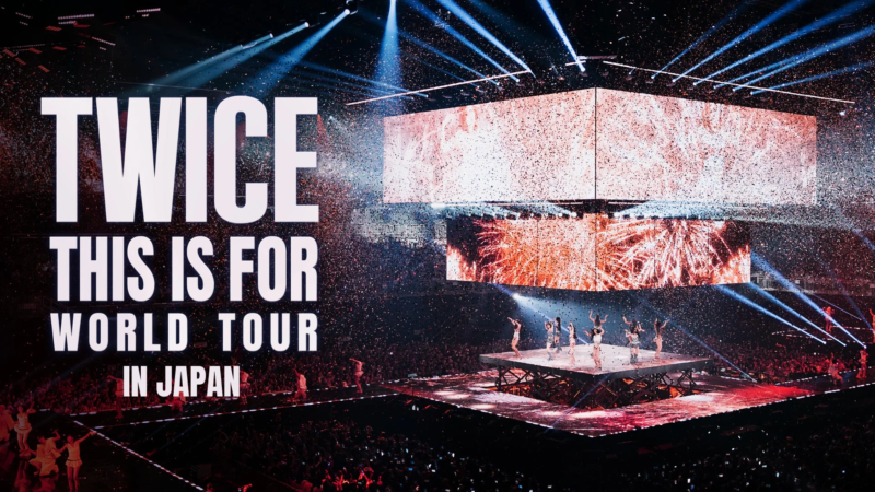 TWICEのワールドツアー日本公演の様子を捉えた画像です。ステージではメンバーがパフォーマンスしており、会場には多くの観客が詰めかけ、紙吹雪が舞い、鮮やかな照明がコンサートを盛り上げています。