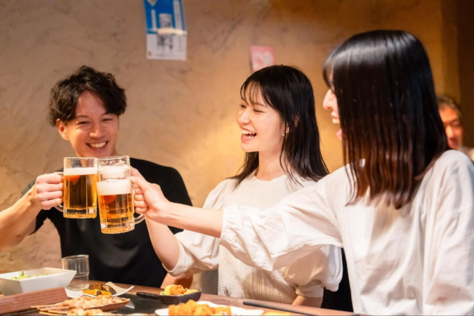 友人同士と思われる3人が居酒屋でビールジョッキを手に乾杯している様子