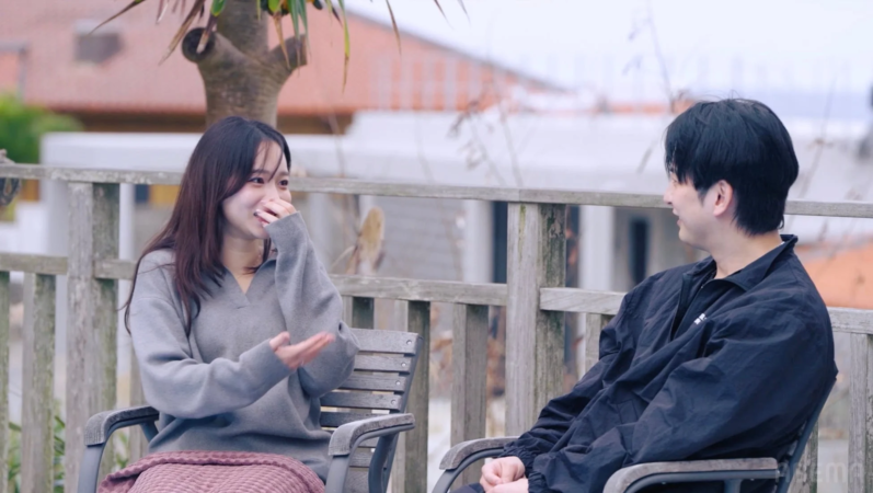 屋外のテラスで男女が向かい合って座り、会話を楽しんでいる様子です。