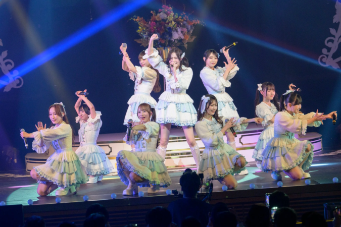 ステージでパフォーマンスを行う9人の女性アイドルグループ