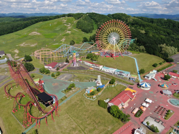 広大な敷地に観覧車や複数のジェットコースターが設置された遊園地の空撮写真