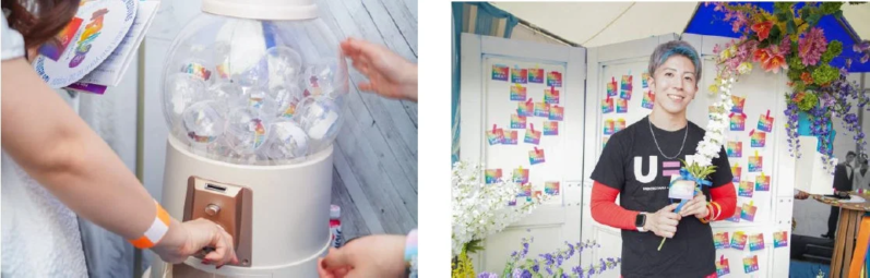 虹色の装飾が施されたイベント会場で、笑顔の男性が花束を持ち、人々がガチャガチャを楽しんでいます。