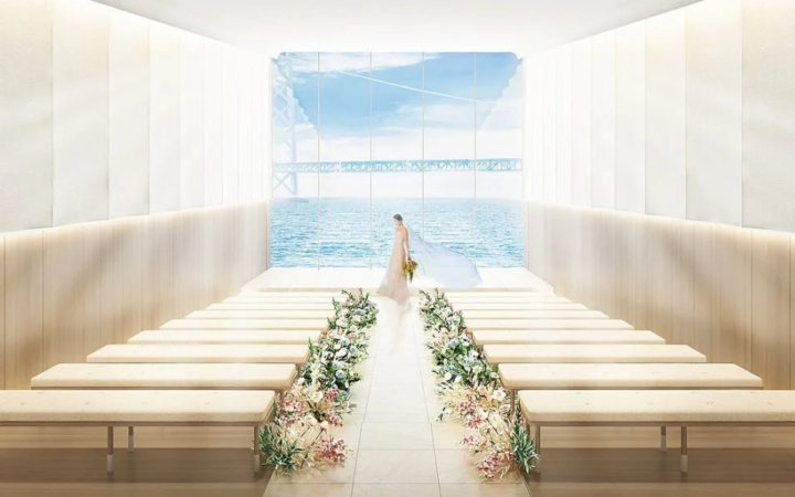 海と橋が見える明るいチャペルで、花嫁がブーケを持ちながらバージンロードを歩く美しい結婚式の風景。