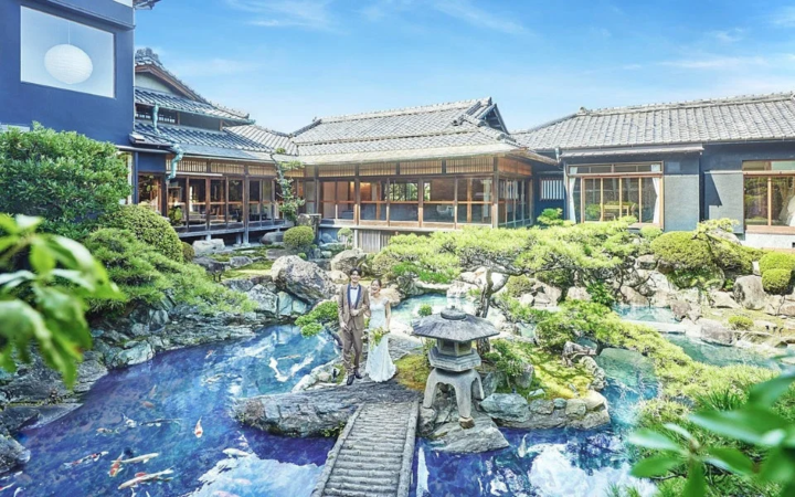 美しい日本庭園を背景に、ウェディング衣装のカップルが石橋の上に立っている様子。