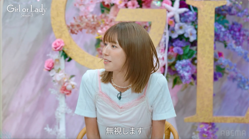 ショートヘアの女性がパールネックレスと白Tシャツ、ピンクのキャミソールを着用し、スタジオで左方向を見ている様子