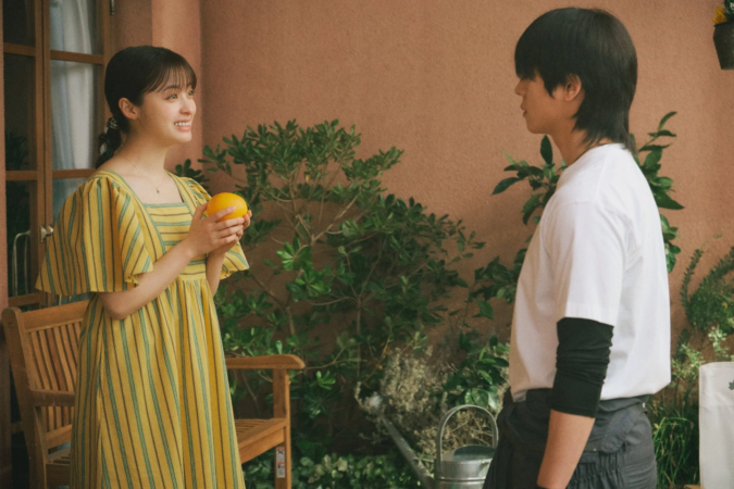 屋外で笑顔の若い女性がオレンジを手に若い男性と向かい合って話している様子