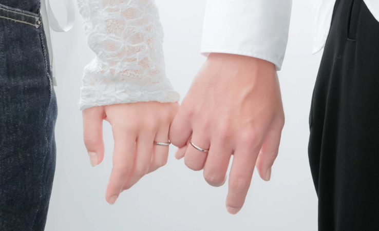 結婚指輪をはめた男女が小指を絡ませて約束を交わしている様子を捉えたクローズアップ写真です。