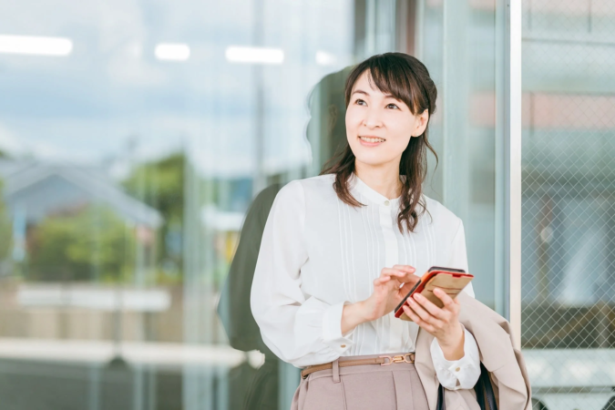 屋外でスマホを操作し笑顔を見せる日本人女性