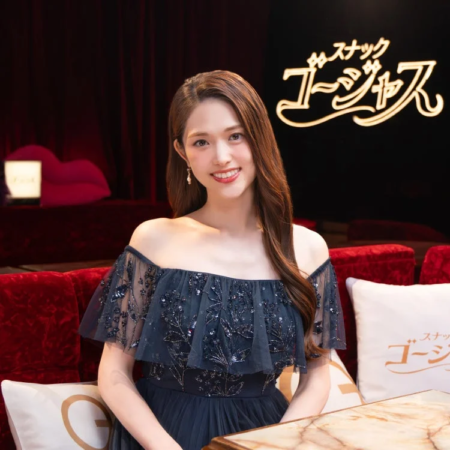 豪華なセットの中で、ネイビーのオフショルダードレスを着た松村沙友理さんが笑顔で座っている