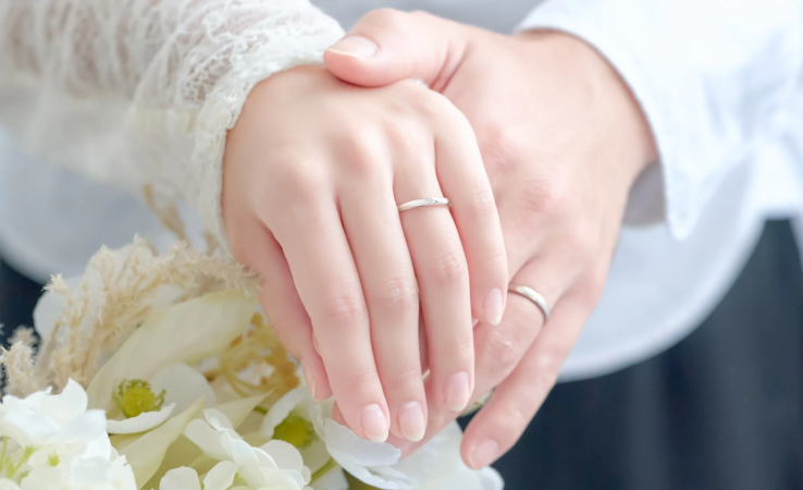 結婚指輪をはめたカップルの手が、白い花束を優しく重ねて握っているロマンチックな一枚です。