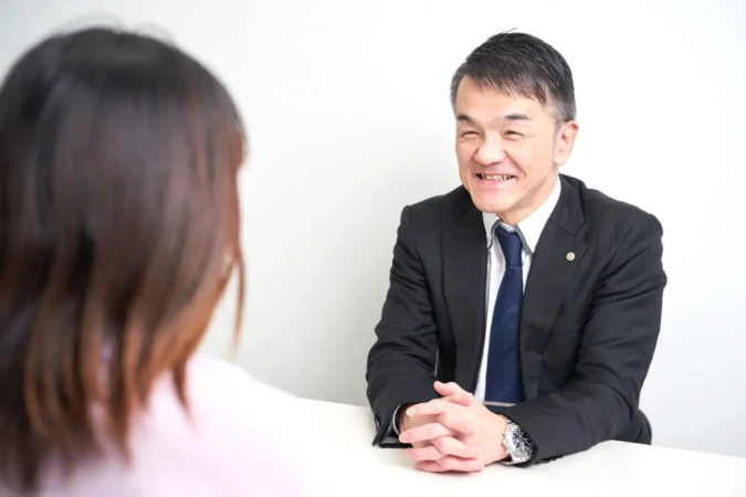 スーツを着た男性が笑顔で相手と会話しているビジネスシーン。面談や商談の様子。