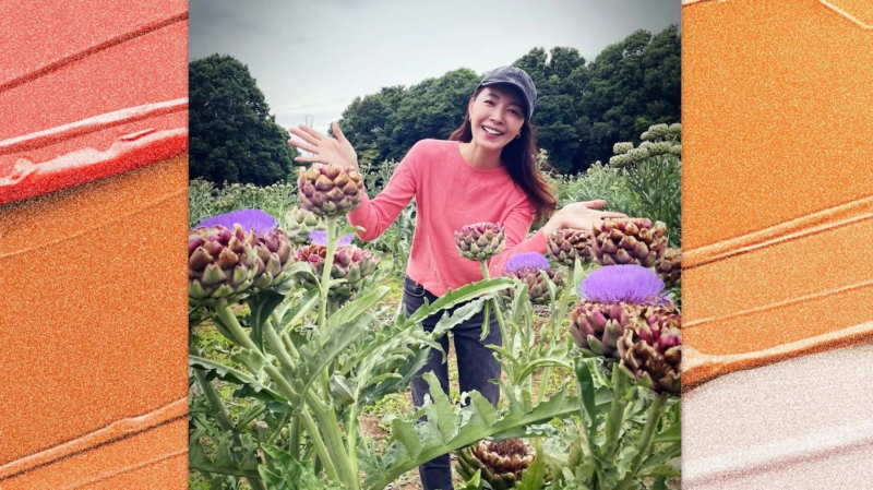 アーティチョーク畑で笑顔の女性が、ピンクのトップスとキャップを身につけ、楽しそうに両手を広げている