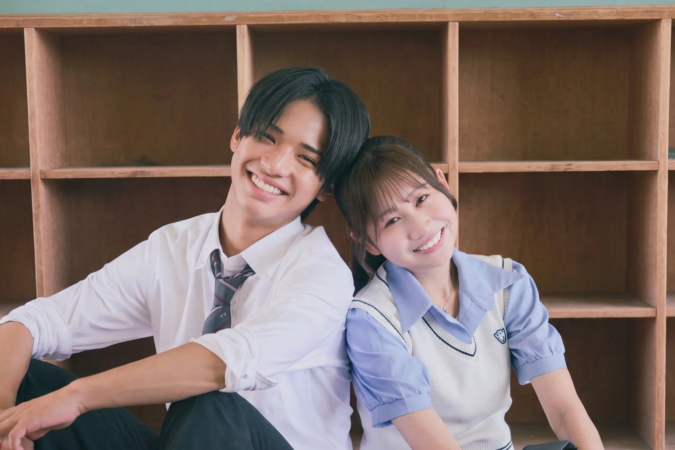 笑顔で寄り添う若い男女の学生が、木製の棚を背景に座っている