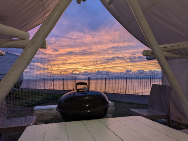 テントの中から夕焼け空と海を望むバーベキューグリル